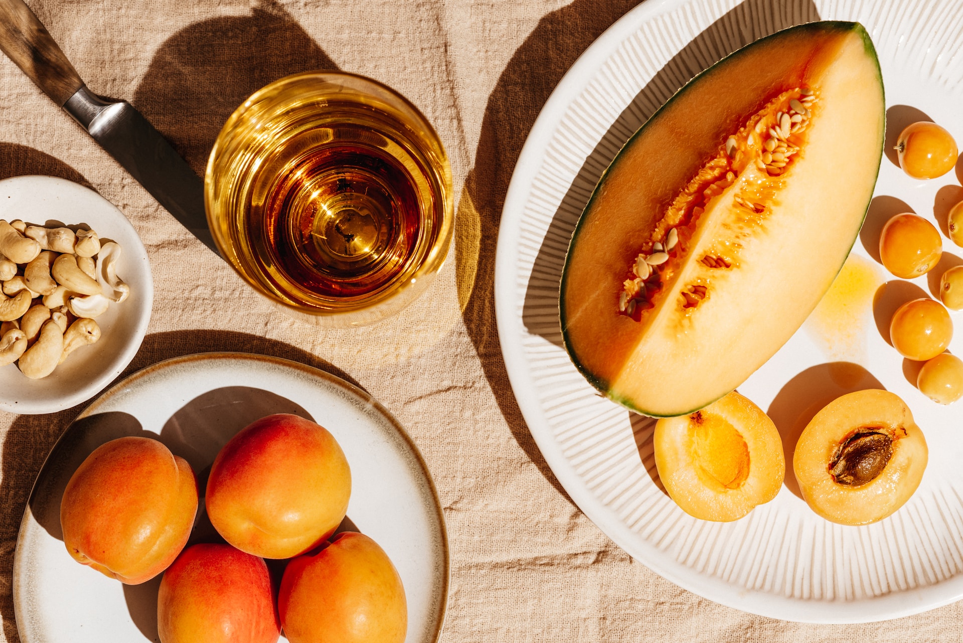 pretty orange fruit on a peach table cloth with a glass of clear orange liquid