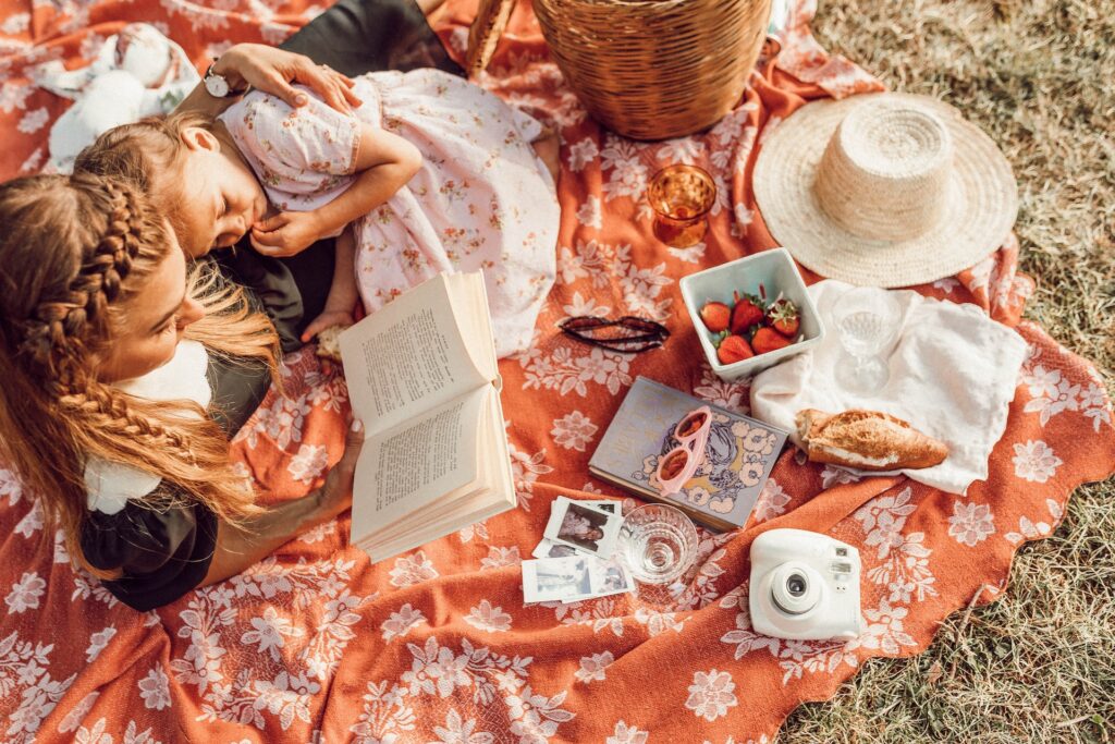 lady sitting on blanket reading a book to her daughter.