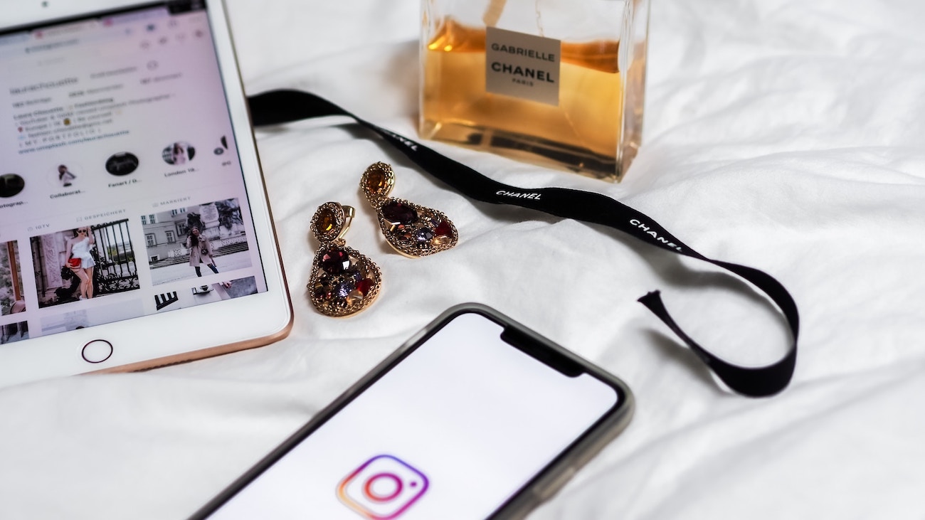 instagram on tablet and iphone. perfume bottle channel. earrings. all on bed zoomed in super cute