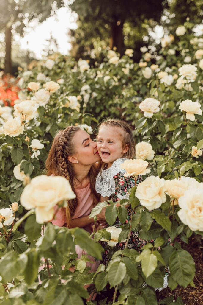 woman kissing daughter on cheek surrounded by flowers.